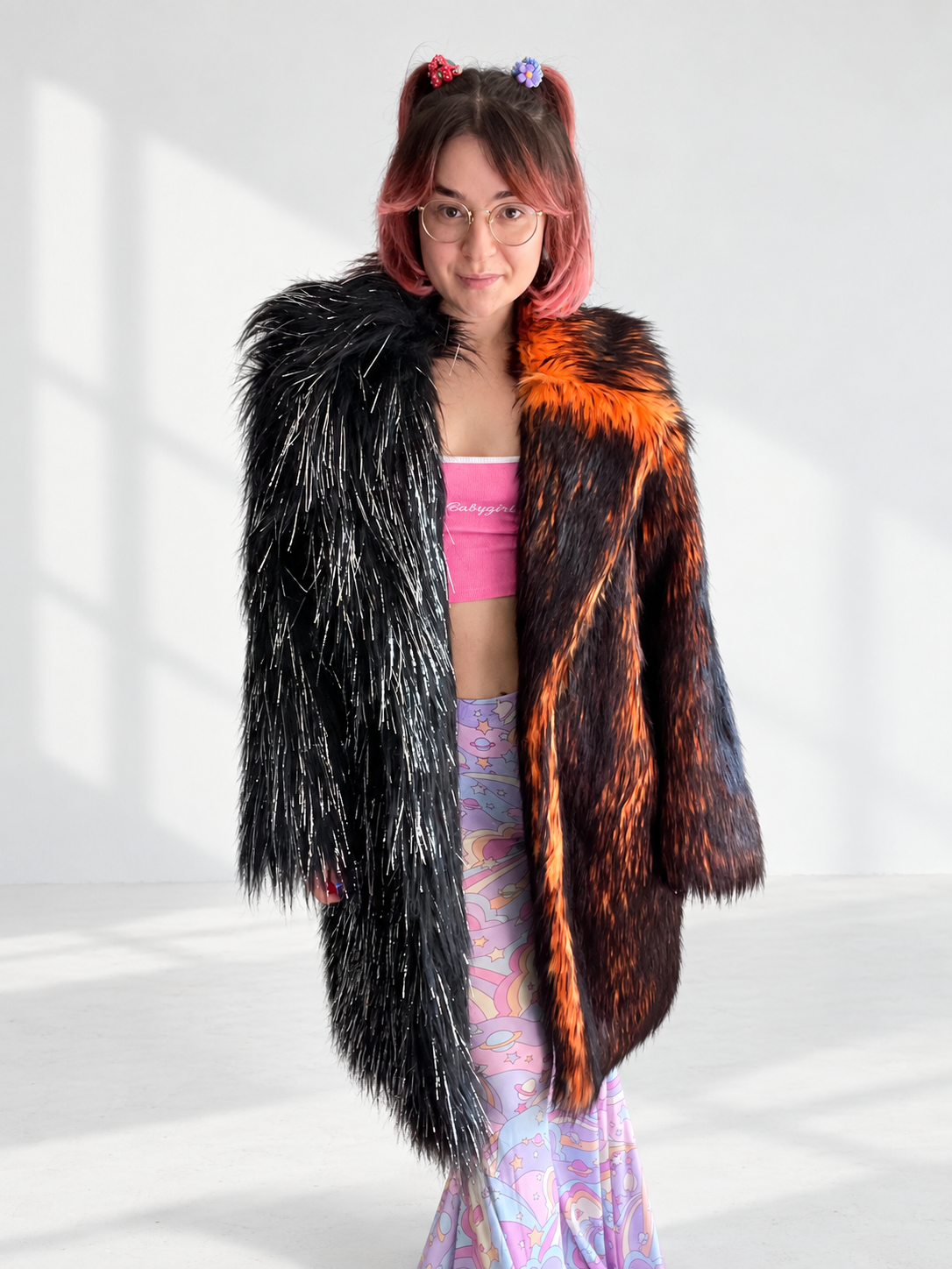 A split-color faux fur coat with one side in vibrant orange and black fur and the other in black shiny tinsel fur  featuring a large circular sun and moon design made with hand-sewn rhinestones on the back.
